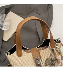 Detail of woven straw bucket bag featuring brown leather handle and metal lock decoration