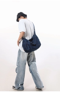 Side view of large washed denim crossbody bag worn by model in a studio setting