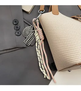 Detail of woven rope charms with metal abacus and racket on a beige straw bucket bag
