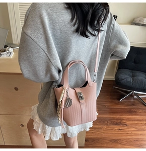 Detail of pink woven bucket bag with metal lock, silk scarf and charm accessory