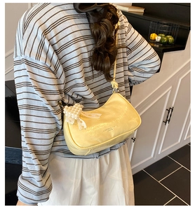 Detail of yellow crescent bag with pleated finish and pearl bow charm on model