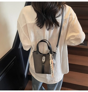 Detail of grey bucket bag with woven texture, metal buckle and decorative pendant charm