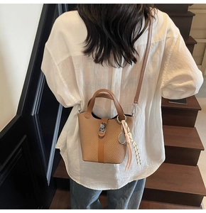 Detail of tan woven bucket bag featuring metal twist lock and tennis racket tassel charm