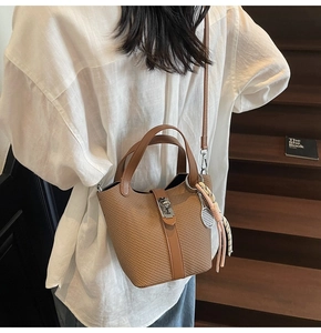 Detail of a brown woven texture bucket bag with tennis racket charm and silver metal lock