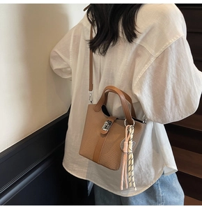 Brown textured bucket bag shown with silver lock buckle and woven charm on a model