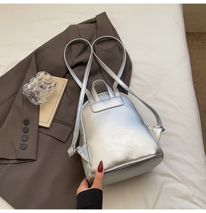 Detail of silver metallic quilted mini backpack on fabric with modern lifestyle props