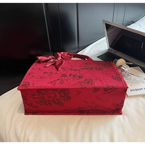 Close-up of red jacquard floral tote bag with branded silk scarf bow on white bedding