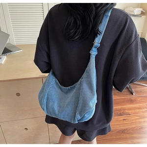 Detailed view of light blue washed denim hobo bag worn crossbody by a model in a room