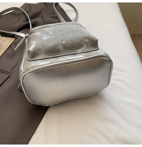 Detail of silver metallic mini backpack featuring quilted texture and rhinestone embellishments