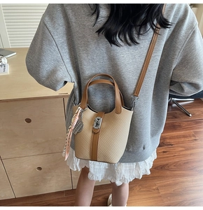 Detail of woven bucket bag featuring brown leather trim and silver lock closure