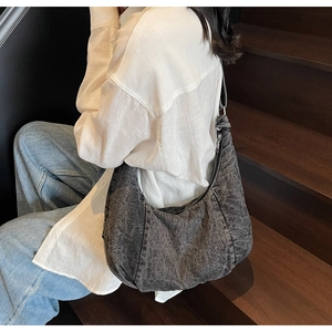 Detailed side view of large washed denim crescent bag worn by model on wooden stairs