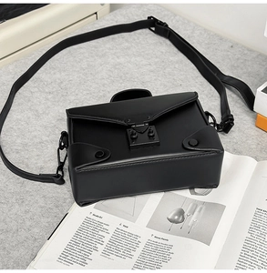 Detail of a structured black square crossbody bag with a matte finish and push-lock closure