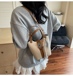 Detail of beige woven straw bucket bag featuring brown leather trim and metallic lock closure