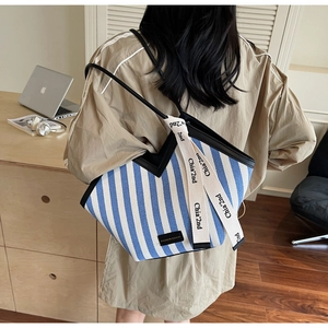 Detail of blue and white striped tote bag with black leather straps and fashion ribbon