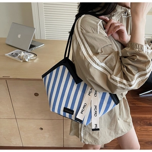 Detail of blue striped canvas tote bag with leather trim and decorative ribbon strap