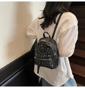 Detail of a mini black quilted backpack with silver studs worn by a model in a casual setting