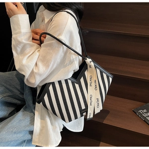 Detail of black and white striped canvas tote with leather straps and logo ribbon accessory