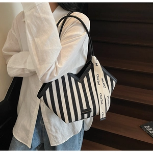 Detail of a large black and white striped tote bag with V-shaped cut and decorative ribbon