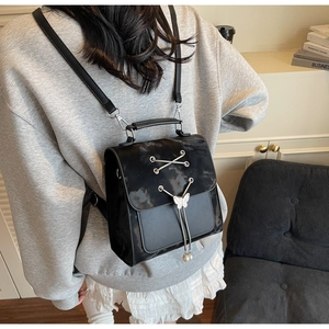 Detail view of black PU leather backpack with butterfly charm and pearl chain decoration