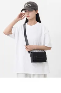 Detail showing matte black square crossbody bag with wide shoulder strap and metal hardware