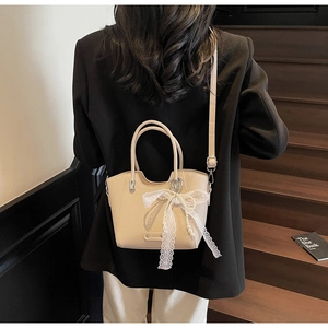Détail du sac fourre-tout beige avec nœud en dentelle et chaîne de perles sur escalier