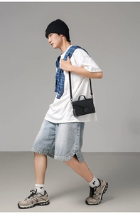 Detail of black PU crossbody bag with metal buckle shown on a walking male model
