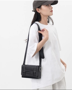 Close-up of a black leather rectangular crossbody bag with stud detail and wide strap