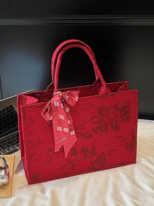 Red floral brocade wedding tote bag with decorative Xi character ribbon on white table