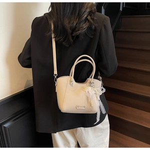 Détail du sac cabas en cuir beige avec breloque nœud en dentelle et perle et logo argenté