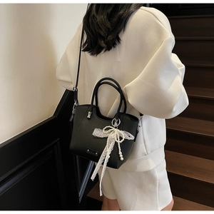Détail d'un sac cabas en cuir grainé noir avec boucle argentée et charm nœud en perles