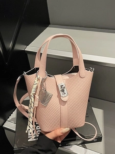 Pink woven bucket bag with metal lock and top handles in a stylish handheld pose