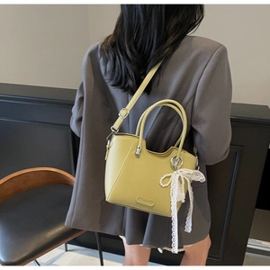 Détail du sac en cuir jaune avec nœud en dentelle et perle sur un costume gris