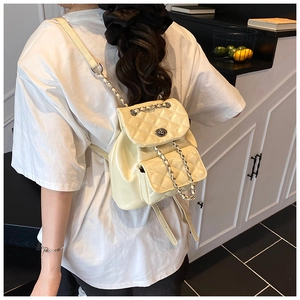 Detail of creamy white quilted patent leather backpack with metal turn-lock and chain strap