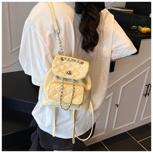 Detail of a beige quilted chain backpack with a turn-lock closure on a model