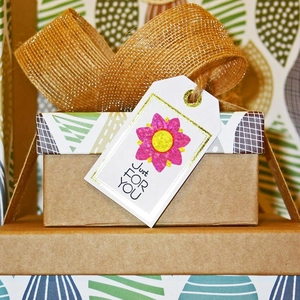 Detail of floral laser gift stickers on a kraft box with a gold glitter ribbon and tag