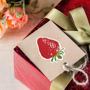 Strawberry stickers on kraft tags with festive red gift box and gold ribbon decor
