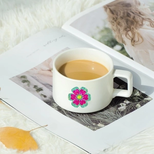 Ceramic flower coffee mug with square handle on a plush rug and magazine background