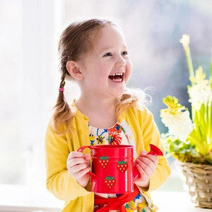 Kids red metal watering can with strawberry glitter pattern held by a smiling young girl