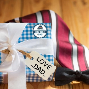 Detail of Father's Day gift box with 'Best Dad' sticker and elegant ribbon on wood surface