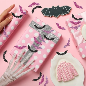 Close-up of holographic bat-shaped Halloween stickers on pink gift wrapping paper
