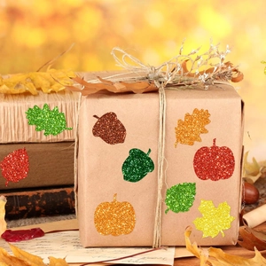 Detail of glitter maple leaf stickers with autumn pumpkins on a gift box setup