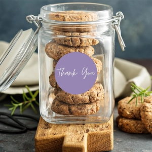 Macro detail of 'Thank You' stickers sealing a glass jar filled with oatmeal cookies