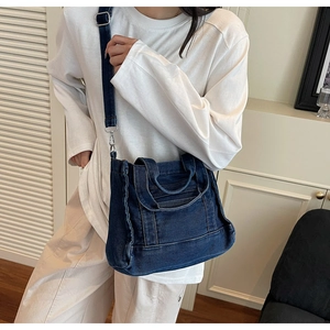 Detail of dark blue denim crossbody bag with adjustable strap and vintage frayed edges
