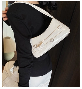Detail of cream white patent leather shoulder bag with decorative bows and metal buckles
