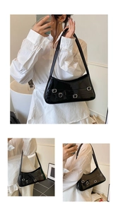 Close-up of black patent leather underarm bag featuring metallic buckles and bow details