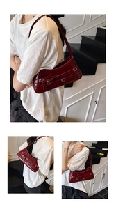 Detail of burgundy patent leather shoulder bag with metallic bow buckle on model