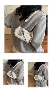 Detail of creamy white underarm bag with crocodile texture, silver chain and sphere charm