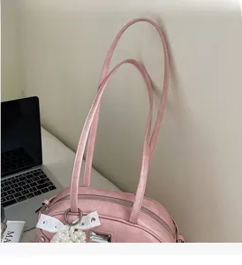 Détail d'un sac à main en cuir verni rose clair avec breloque perle et décor dentelle