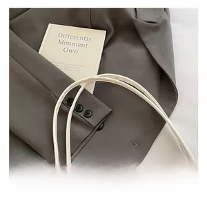 Close-up of sleek white leather handbag with rounded handle against a grey blazer
