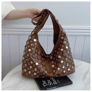 Détail d'un sac seau en cuir marron avec œillets et rivets argentés sur un livre noir